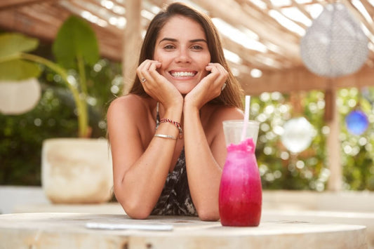A smiling woman sitting outdoors enjoying an antioxidant-rich pink smoothie for healthy skin and sun protection.